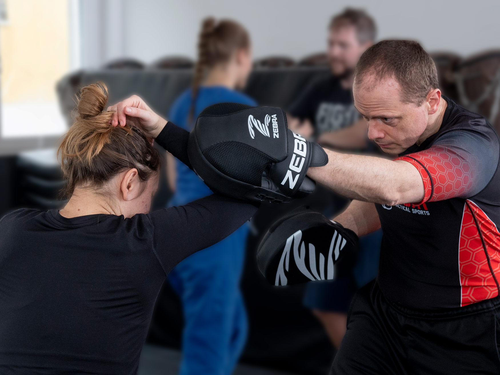 Frau trainiert Krav Maga Selbstverteidigung mit Trainer an Schlagpolstern in einer Kampfsportschule.